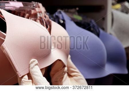 Woman Chooses Wireless Bra Hanging On Rack In Lingerie Store, Female Hands In Protective Gloves. Con