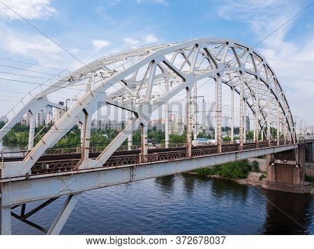 Span Of The Railroad Bridge With Steel Riveted Arch Truss Over The River Against The City Buildings