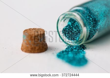 party, decoration and holidays concept - close up of blue glitters poured from small glass bottle and cork stopper over white background