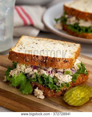 Tuna Fish Salad And Lettuce Sandwich On Multiseed Bread With Sliced Pickles On A Wooden Cutting Boar