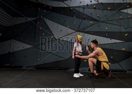Male Instructor Teaching Little Girl To Use Climbing Equipment, Showing How To Use A Carabiner For B