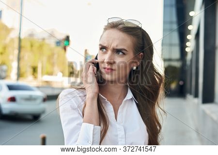 The Gloomy Girl Is Talking On The Phine. The Girl With Phone Is In Hurry. The Girl Is Near A Busines