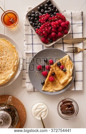 Flat layout of kitchen table served for breakfast with fresh berries, appetizing pancakes, sourcream, honey and chocolate spread
