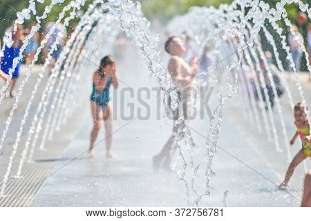 Children Play In Dry Fountain. Little Kids Playing In Waterspouts. Blurry Silhouettes. Exciting And 