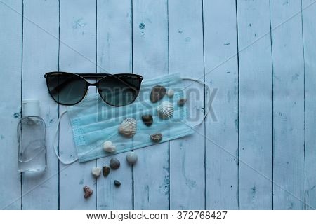 Sunglasses, Pebbles, Medical Mask And Antiseptic On A Wooden Background. The Tourist Crisis In The S