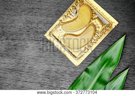 Gold Cosmetics Hydrogel Patches And Green Leaves On A Black Wooden Background With Copy Space. Skin 