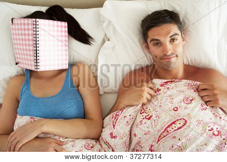 S'ennuyer à la recherche de l'homme couché dans son lit à côté de la femme lecture livre