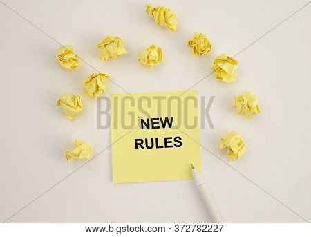 Text New Rules Written On Yellow Note Paper On White Table With Wrinkled Papers Around. New Rules Co