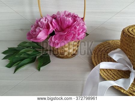 Pink Peonies In A Wicker Straw Basket And Wicker Straw Hat On A Light Wood Background