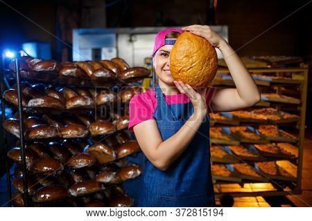 The Stage Of Baking In A Bakery. Portrait Of A Baker Girl With Bread In Her Hands Against The Backgr