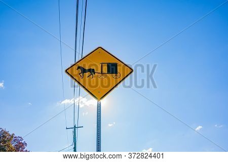 Sun Shines From Behind Amish Traditional Horse And Buggy Road Sign In Lancaster County Pennsylvania,