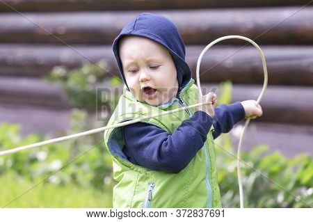 A Child Dressed In A Vest And Hoodie Stretches An Electric Wire Against The Background Of A Log Hous