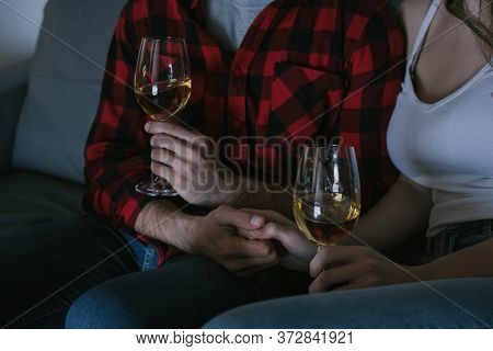 View Of Couple Holding Hands While Sitting On Sofa With Glasses Of White Wine