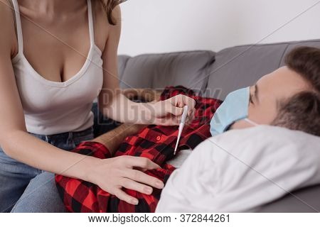 Cropped View Of Young Woman Holding Thermometer Near Sick Boyfriend Lying On Sofa In Medical