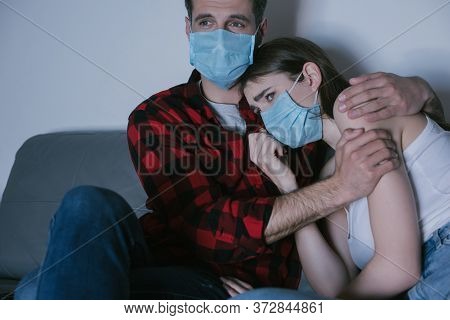 Couple In Medical Masks Watching Tv While Man Hugging Sad Girl