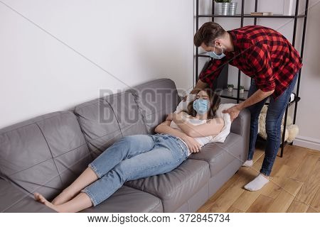 Man Touching Pillow While Sick Girlfriend Lying On Sofa In Protective Mask