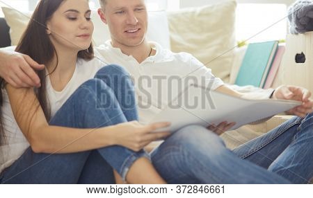 Young couple moving in to new home together, sitting on The floor and diskuss plan of desing.