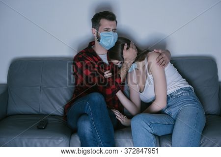 Couple In Medical Masks Watching Tv While Man Calming Upset Girl