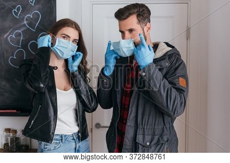 Couple In Latex Gloves Putting On Protective Masks Before Leaving Home