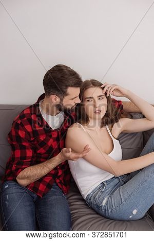 Man Showing Shrug Gesture While Sitting On Sofa Near Depressed Girl