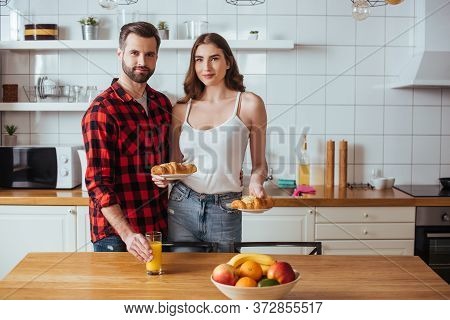 Girl Holding Plates With Delicious Croissant Near Boyfriend Touching Glass Of Orange Juice