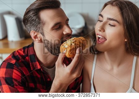 Man Biting Croissant Near Girlfriend With Open Mouth And Closed Eyes
