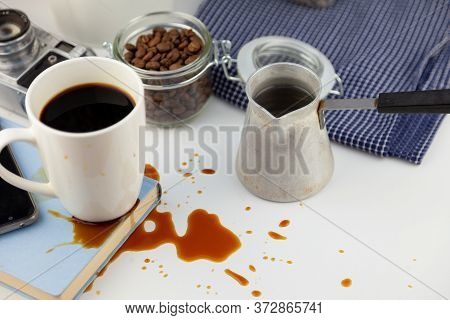 Coffee Spilled On A Book On The Desktop. A Cezve For Coffee, Coffee Beans, A White Cup Of Coffee, Sp