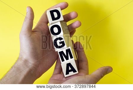 The Word Dogma From Building Blocks Is Held By A Man On A Yellow Background