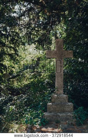 London, Uk - June 16, 2020: Stone Cross On A Tomb Against Greenery Inside Hampstead Cemetery, A Hist