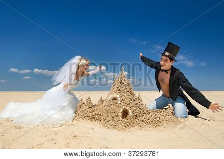 En ung och vacker nyligen gift par njuter på stranden nära sand slott vid havet kanten