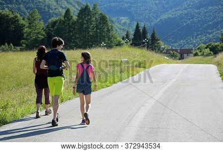 Mother With Two Young Children While Walking On The Asphalt Road