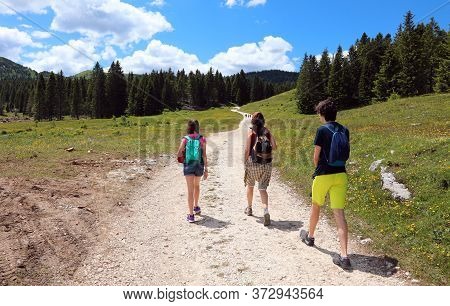 Family Of Three With Mom And Daughter And Son While Walking On The Road In The Mountains In Summer