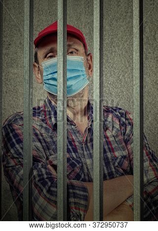 Man In Mask And Red Hat Arrested For Quarantine Violation. He Stands In A Pretrial Detention Cell Wi