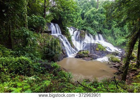 Waterfall Landscape View Of Fresh Water Flows Over A Vertical Drop To Green Field In Tropicana