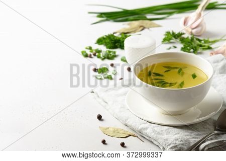 Chicken Broth With Spices, Greens, Garlec, Parsley, Onion In White Bowl On White Table. Copy Space. 
