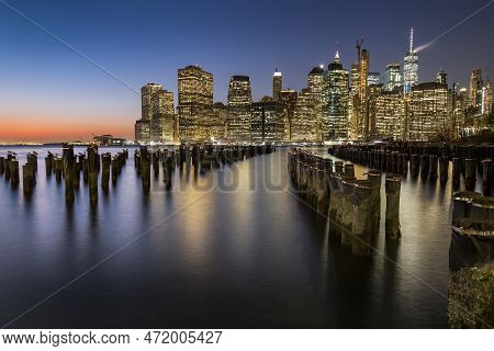 View Of Lower Manhattan At Dusk Seen From Brooklyn. Remaining Of An Old Pier Can Be Seen At The Fore