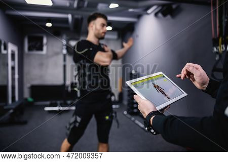 Stretching The Arm Muscles And Showing The Performance On A Special Ems Tablet. A Man In A Special S