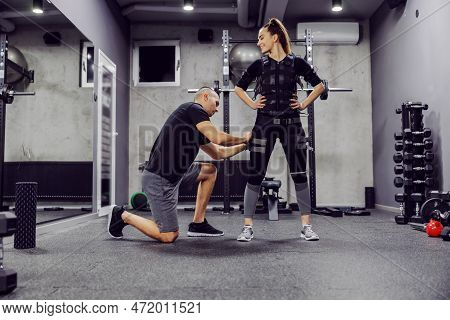 The Concept Of Revolutionary Training. The Male Coach Helps The Slender Woman Around The Ems Suite I