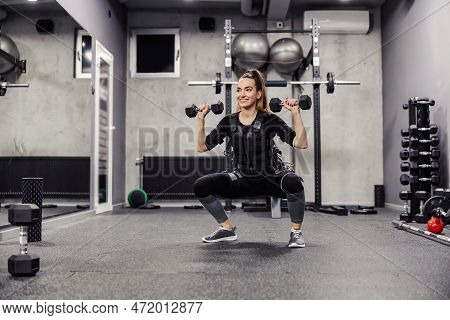 Electrical Muscle Stimulation. A Young And Healthy Woman In A Special Black Ems Suit Performs Squats
