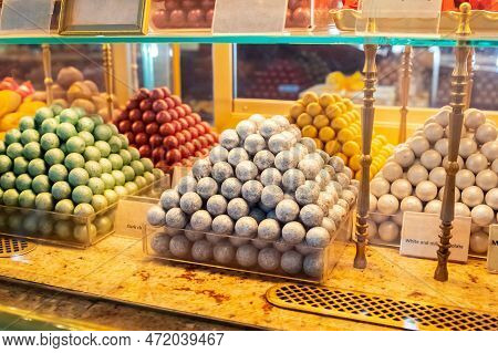 Hand Crafted Chocolate Bites A Lot On Shop Window, Store Shelf. Heap Of Assorted Chocolates. Candy B