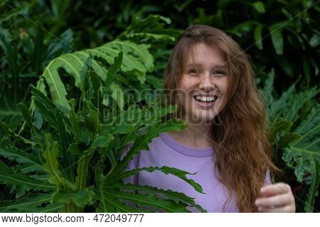Portrait Of Young Woman Standing On An Ivy, Fern Wall Or In Greenery, Breathing, Smiling And Looking