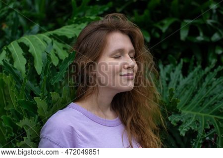 Portrait Of Young Woman Standing On An Ivy, Fern Wall Or In Greenery, Breathing, Smiling And Looking