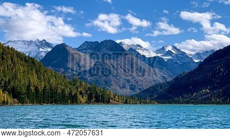 Snow-capped Mountain Peaks In The Foreground Is A Blue Lake With Clear Water.