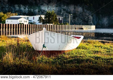 An East Coast White Dory Laying On A Grassy Shore With A Distant Breakwater At Placentia Newfoundlan