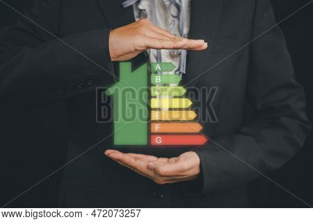 Business Woman Hand Holding House Icon Energy Efficiency Scale Image On Virtual Screen, Concept Of E