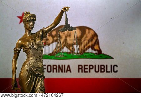 Close-up Of A Small Bronze Statuette Of Lady Justice Before A Flag Of California.