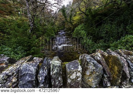 Uk River In Autumn Fall With Top Of Dry Stone Wall Of Bridge In Foreground.