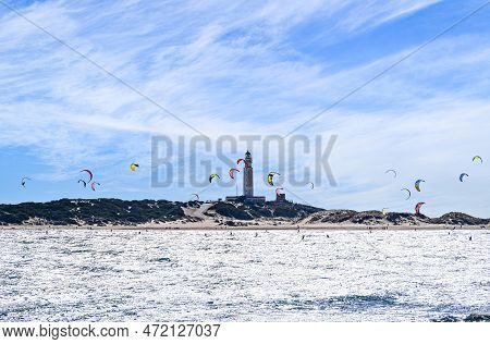 People Practicing Kitesurfing On The Beach Of Los Caños De Meca, Next To The Trafalgar Lighthouse, B