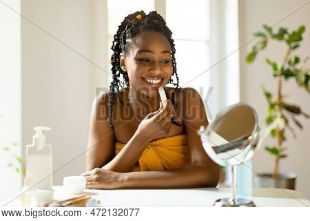 Happy Beautiful Black Woman Using Moisturizing Lipbalm, Lady Sitting At Vanity Table, Looking At Sma