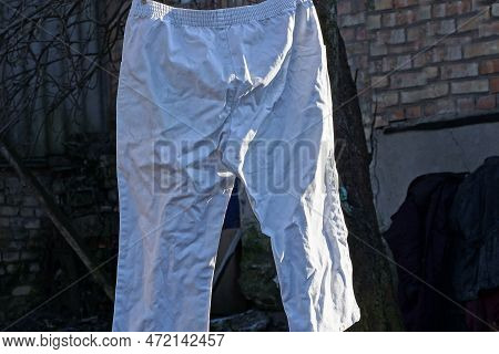 One White Crumpled Cloth Pants Hangs On A Wire In The Street